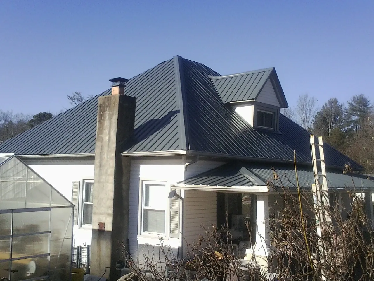 Dark blue standing seam metal roof on a white farmhouse with dormer — Slate & Tile Roof Repair by Roofing Brothers in Saint Anthony