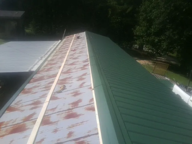 Old rusted panels beside newly installed green metal roofing — Wind Damage Roof Repair by Roofing Brothers in Saint Anthony