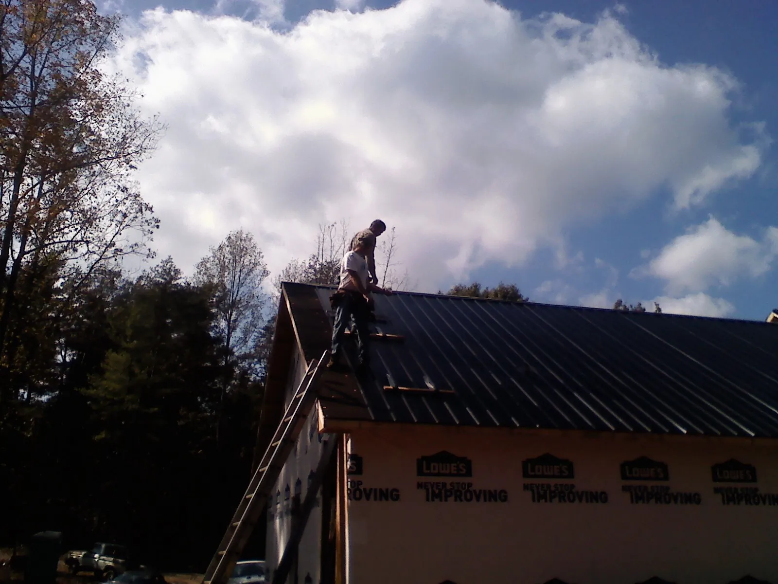 Roofer fastening dark metal panels high against a cloudy sky, from a Roof Inspection job in Saint Anthony