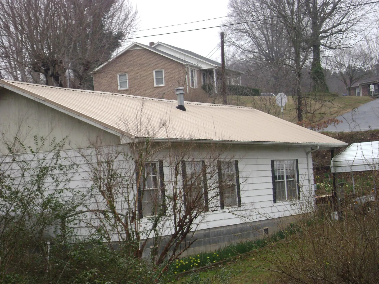 Tan metal roof on a white sided house set into a hillside — Commercial Roofing by Roofing Brothers in Saint Anthony