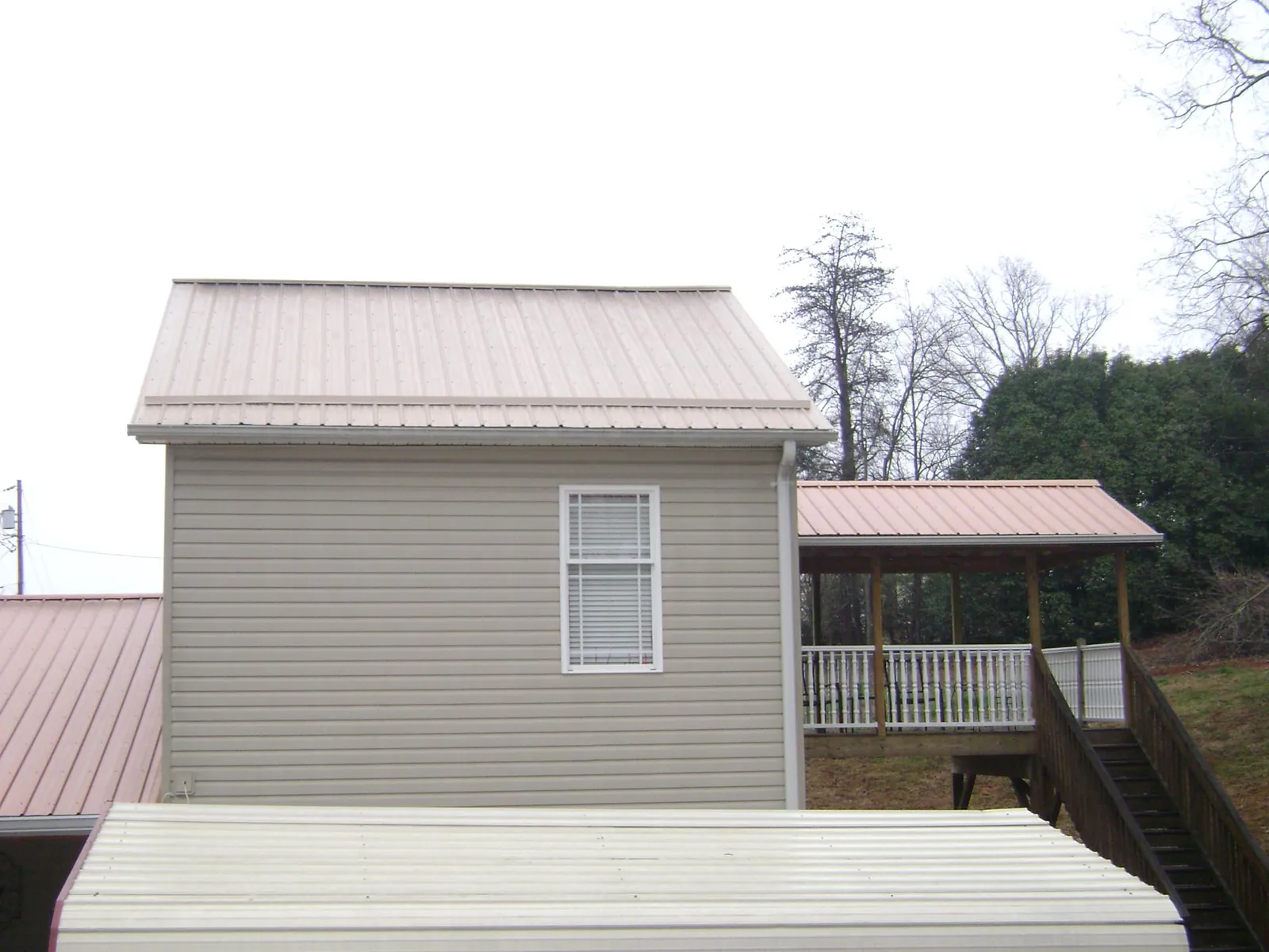 Tan metal roofs on a two story addition and attached porch, from a Roof Replacement job in Saint Anthony
